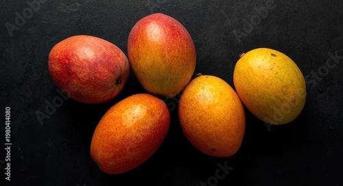 Tropical mangoes featuring bright colors and sweet aroma arranged on black surface