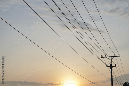 Cuadro en lienzo Image of electric cables and poles, with orange sky background