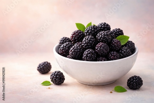 Blackberries arranged in a white ceramic bowl on a soft pastel backdrop with copy space