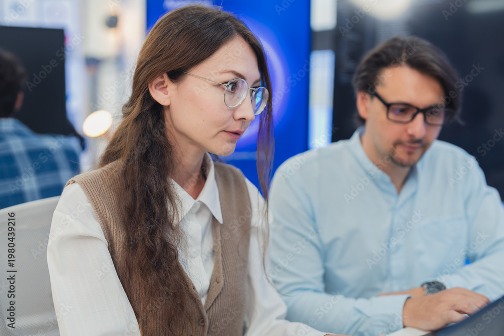 Fototapeta premium Caucasian male and female tech colleagues collaborating on laptop in modern blue-lit AI technology office, perfect for software development, teamwork, and digital innovation concepts.