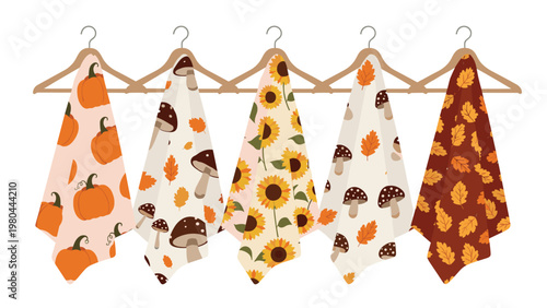 Collection of autumn themed kitchen towels hanging on wooden hangers featuring pumpkins, mushrooms, sunflowers, and falling fall leaves.