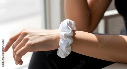 Close up of a woman's arm wearing a white fabric scrunchie on her wrist with a black outfit and natural light background ideal for fashion and accessory advertising