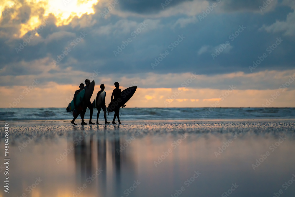 Ταπετσαρία Silhouette of Surfers at Sunset: A group of surfers strides along a sandy beach at dusk, each silhouetted against a radiant, cloud-filled sky reflecting in the wet sand, ready to seize the waves