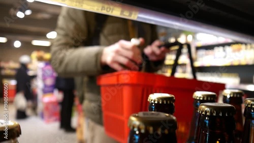 A customer takes two bottles of beer from a retail display and puts them into a shopping basket