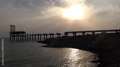 Silhouette of Industrial Pier or Bridge Structure Over Water at Sunset with Dramatic Sky