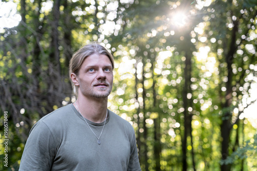 Thoughtful young man in forest sunlight reflecting