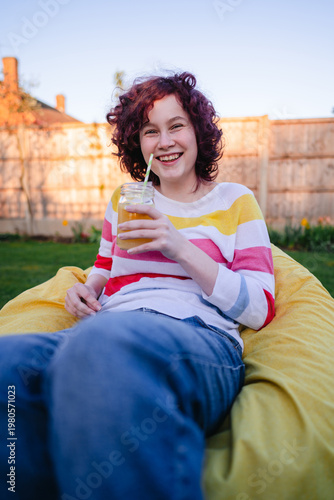 Teen age girl enjoying a lemonade on yellow bean bag in the backyard