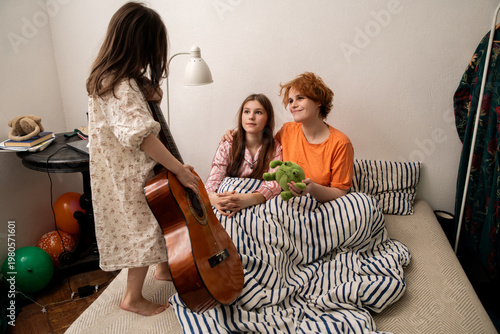 Little girl bringing guitar to bed for mom and sister in cozy morning