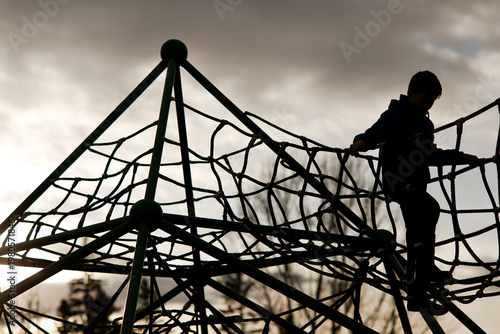 Silhouette of a young boy climbing on a rope playground at dusk