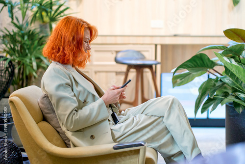 A businesswoman with red hair sitting and using th e mobile phone in co-working space area for relax.