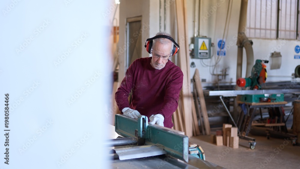 Fototapeta premium Senior carpenter working a planer with wood planks in workshop