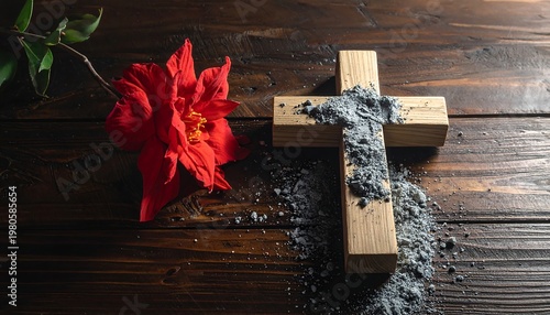 A wooden cross with ash and a red flower on a dark table