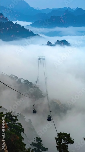 A cable car ascends through a dense sea of clouds, revealing a breathtaking vista of layered mountains in a serene and misty landscape.