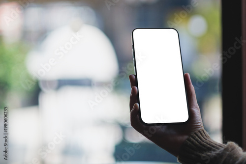 Mockup image of a woman holding and using mobile phone with blank desktop screen