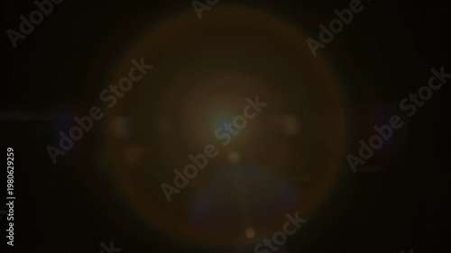 A softly illuminated circular shape glows warmly against a deep black background, creating a sense of mystery and subtle focus.