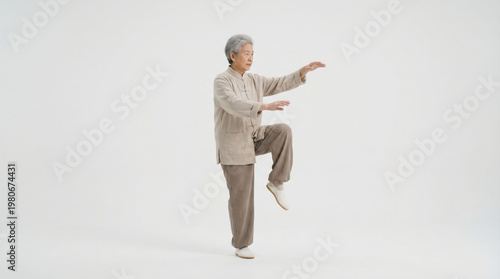 Elderly man practicing tai chi walking pose in traditional clothing with calm expression on white background for wellness and balance