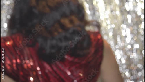 A woman in a shiny dress stands in silhouette against a curtain
