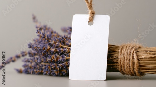 Minimalist product tag mockup with a blank white label hanging from a dried lavender bouquet tied with rustic jute twine on a calm gray background for handmade aromatherapy product branding.