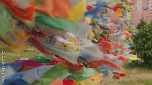 A dynamic and vibrant shot of moving Tibetan prayer flags. The colorful banners, bearing mantras, flutter in the wind. They symbolize peace, spirituality, and hope. The backdrop is urban