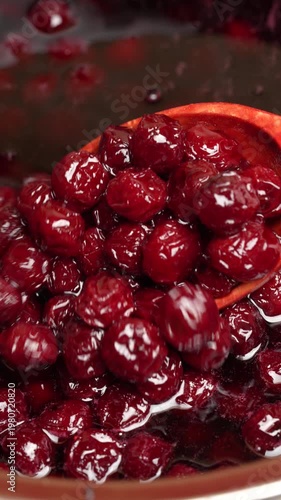 Preparing freshly picked red cherries with sugar to make cherry jam in a saucepan with a wooden spoon, close up. Cooking berries marmalade, home cooking