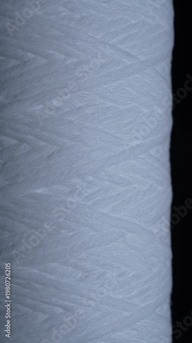 Close up of white polypropylene string wound sediment filter cartridge used for water purification filtration and household plumbing systems, rotates. Texture or background polypropylene water filter