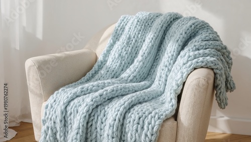 Fotografía Cozy light blue chunky knit blanket draped over a beige armchair, soft natural morning sunlight in home interior
