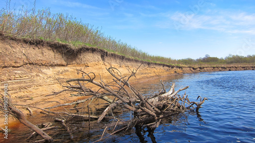 Riverbank erosion shows exposed soil and fallen branches