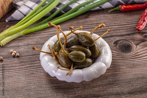Bilde på lerret Pickled caper berries in a bowl with fresh ingredients on a rustic wooden table