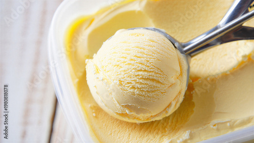 Foto Scooping creamy vanilla ice cream from a plastic tub onto a light wooden backgro