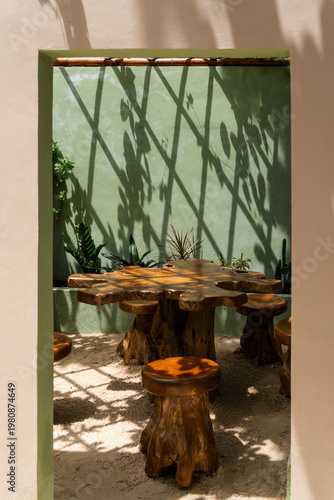 Rustic wooden table and stools standing in a sunny outdoor courtyard with tropical plants
