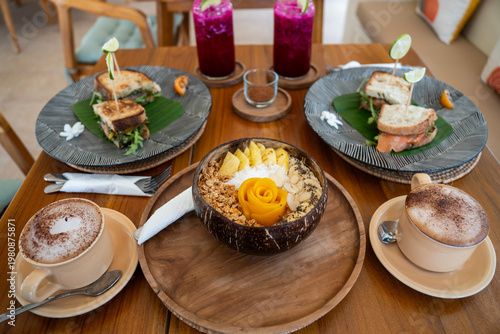 Wooden table filled with a healthy breakfast spread, featuring a smoothie bowl, sandwiches, and coffee