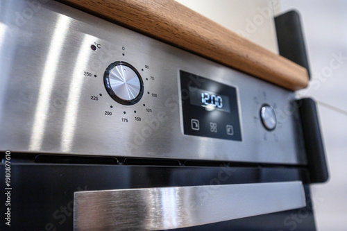 Foto A stainless steel built-in oven with a temperature dial (up to 250°C), digital display showing «12:00», touch buttons, and a sleek wooden countertop above
