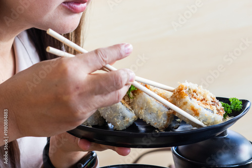 Close-up of a person using chopsticks to eat a crispy Salmon Tempura sushi roll, a vibrant and delicious Japanese lifestyle food photography.
