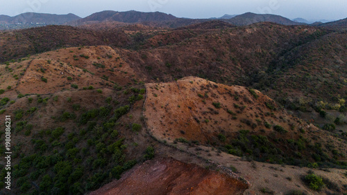 Aerial view of the Aravalli hills near Udaipur, Rajasthan at sunset in spring, showing native vegetation with a cut patch on a hillside for construction.