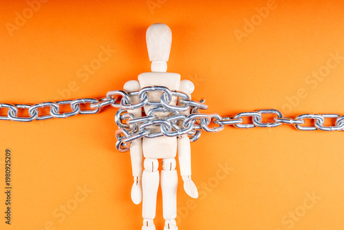 Fotografija A wooden doll on an orange background is fixed with a chain