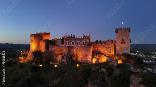 Aerial 4K view of the illuminated Almodovar Castle at night in Cordoba, Spain. Medieval fortress with exterior lights on and scenic night landscape.
