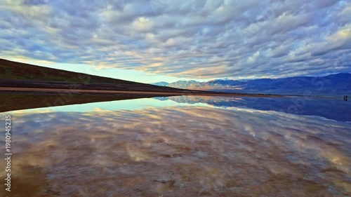 Panoramic mountain range reflecting in still mirror waters at Badwater Basin Death Valley California