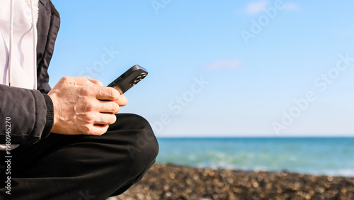 Foto Person in hooded jacket using phone on pebbly beach