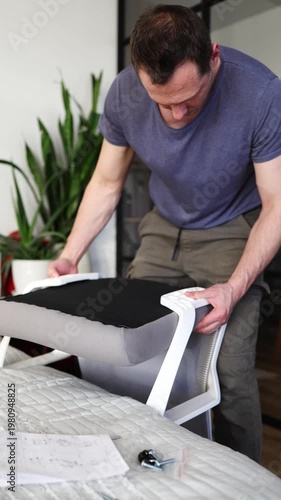 Adult male assembling office chair using hex key tool on wooden floor. Caucasian man hands screw chair lifting mechanism. Assembling office chair.