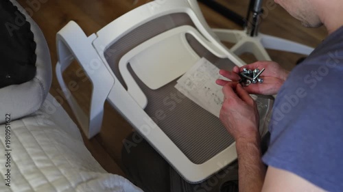 Adult male assembling office chair using hex key tool on wooden floor. Caucasian man hands screw chair lifting mechanism. Assembling office chair.