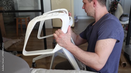 Adult male assembling office chair using hex key tool on wooden floor. Caucasian man hands screw chair lifting mechanism. Assembling office chair.