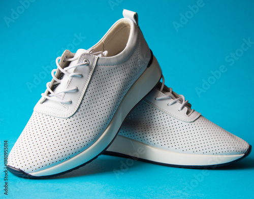 New  pair white sneakers isolated on blue background. Close-up of a stylish walking shoes for workout. Modern design footwear