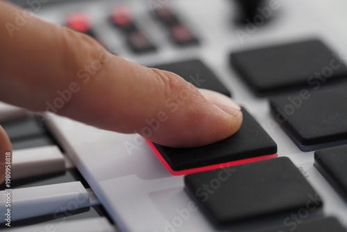 Finger push pads on midi controller, creates music drums. Selective focus.
