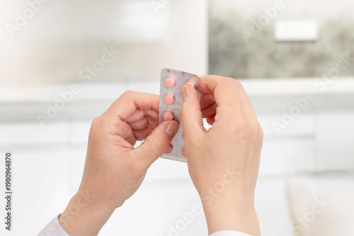 Foto Close up of hands pressing pills from blister pack in home setting, medication u