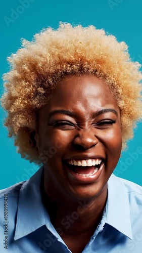 Joyful Young Woman With Curly Blonde Hair Laughing Heartily Against a Blue Background