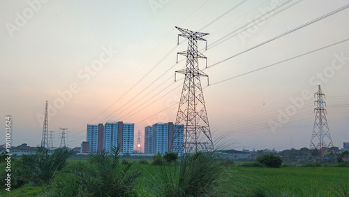 Schilderij op canvas High voltage power transmission tower with electric lines at sunset, urban skyli