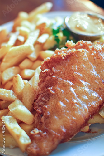 A plate of fish and French fries served with a side of dipping sauce. vertical frame