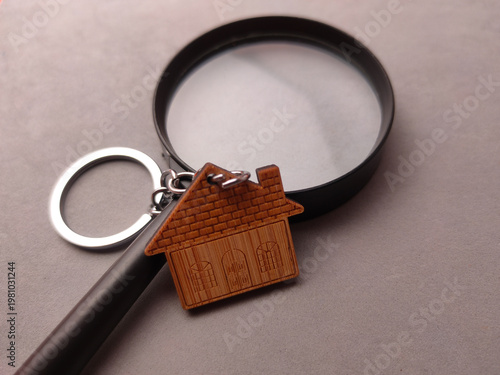 Wooden house shaped keychain resting against a large black magnifying glass