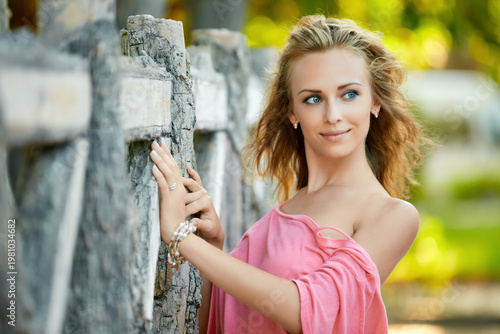Elegant woman in pink top near rustic wooden fence