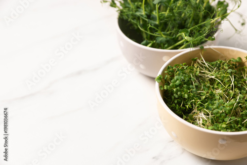 Different types of microgreens on white marble table, closeup. Space for text
